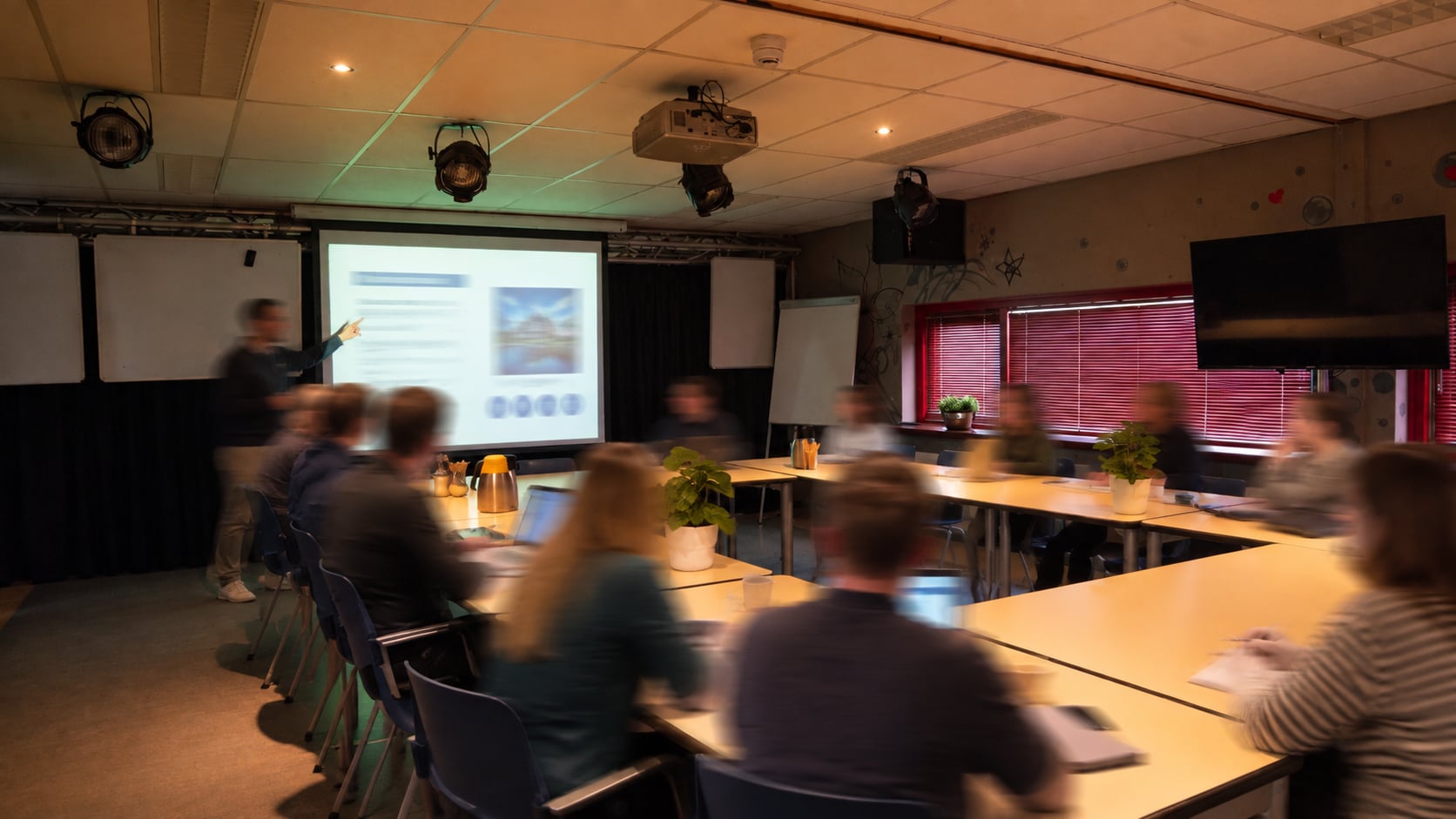 Een cursus in de multifunctionele ruimte: presentatie op het projectiescherm, tafels in U-opstelling